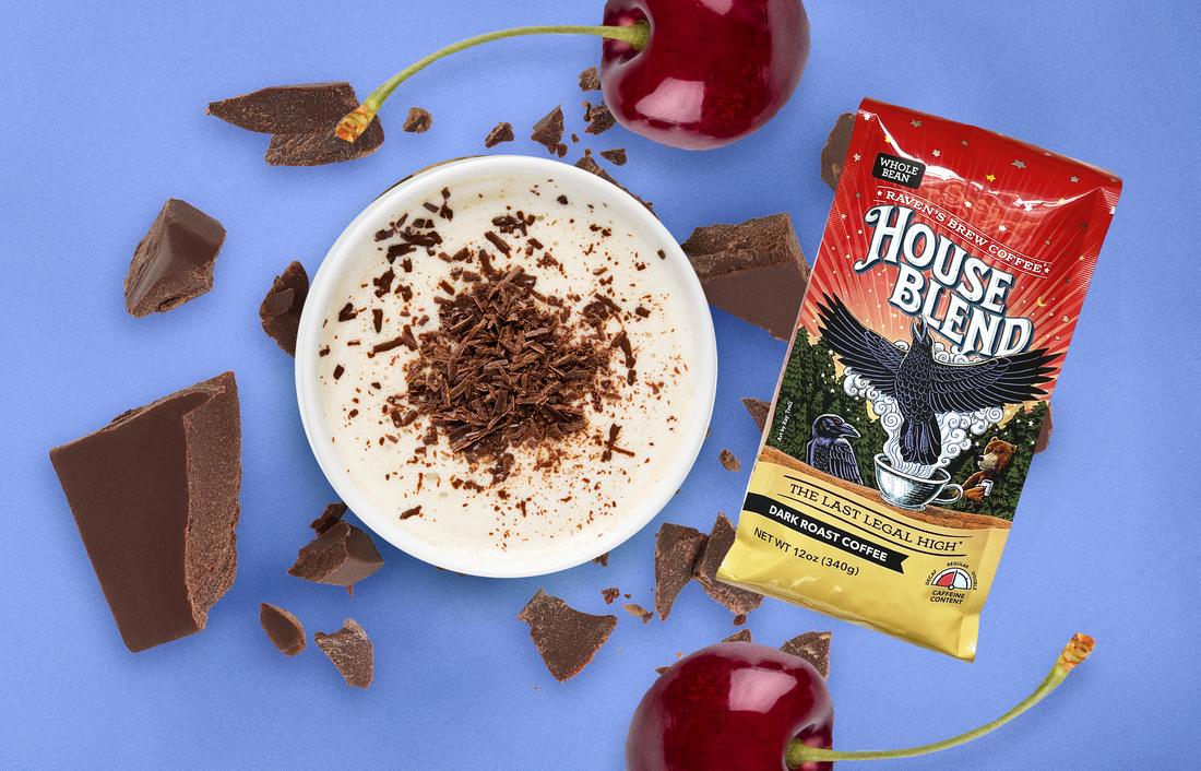 A frothy latte topped with shaved chocolate surrounded by giant chocolate chunks, cherries, and a bag of House Blend Coffee.