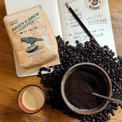 Kraft bag of Roaster's Pick: Seasonal Blend on a table with open sketch book, a pile of beans, a bowl with coffee grounds, and a freshly pulled shot laid on top.