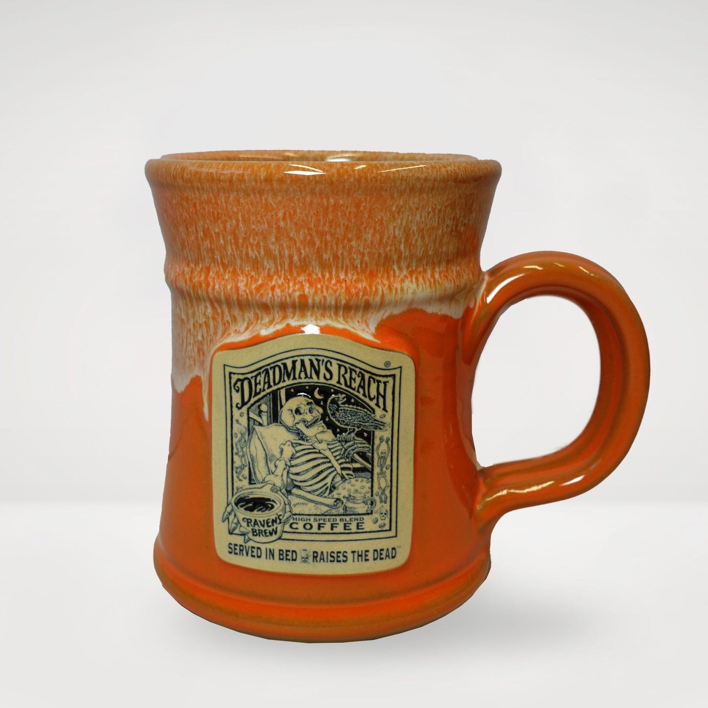 A hand-thrown orange mug featuring the Deadman's Reach® Coffee Label art impressed on the surface.