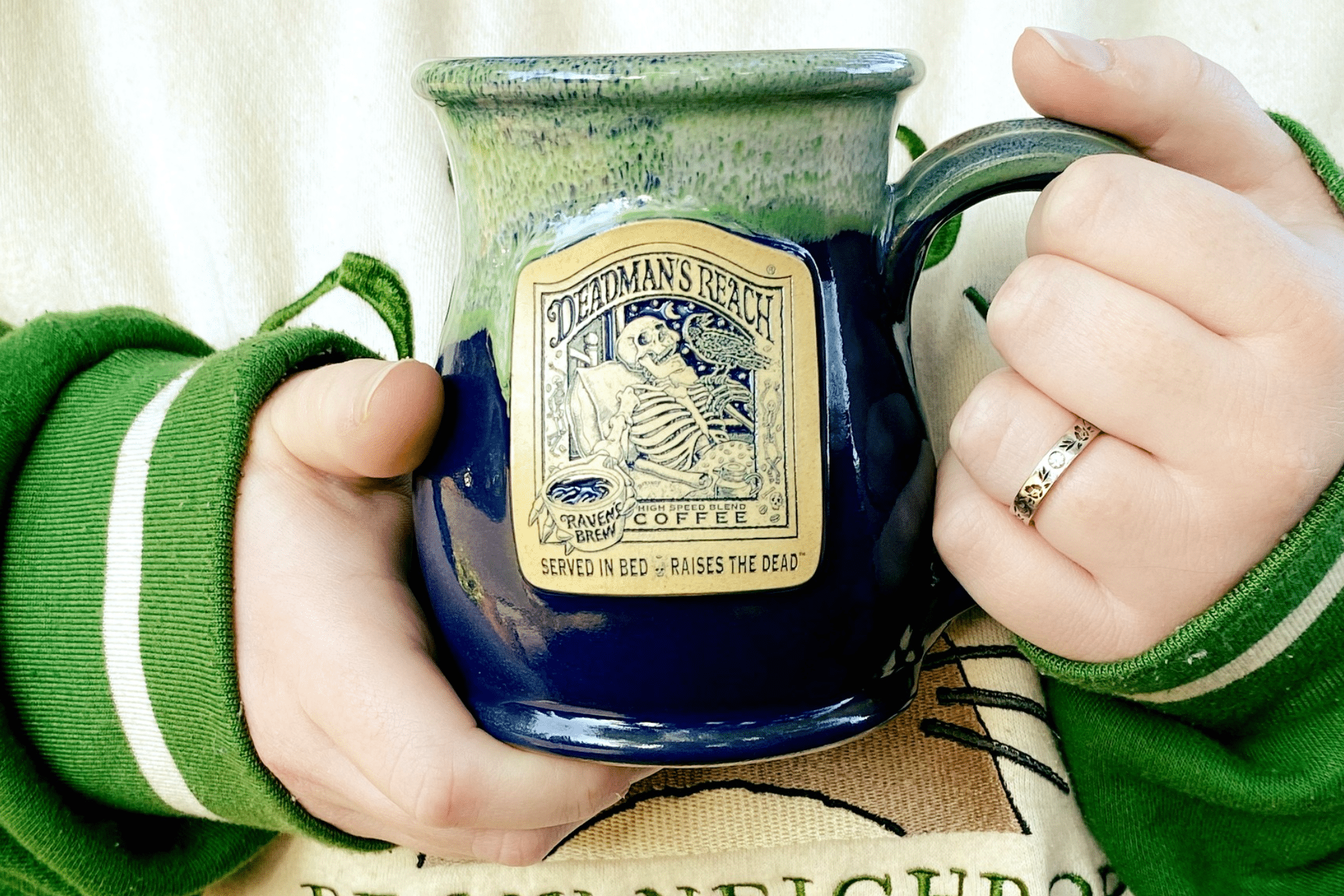 Person holding a warm mug of coffee in a Deadman's Reach Coffee mug