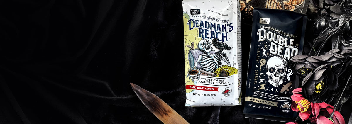 A bag of Deadman's Reach and Double Dead high caffeine content coffees sit upon some black velvet fabric. A small box with a skeleton on it sits behind the coffee, a wooden stake and roses sit in front of the coffee bags.