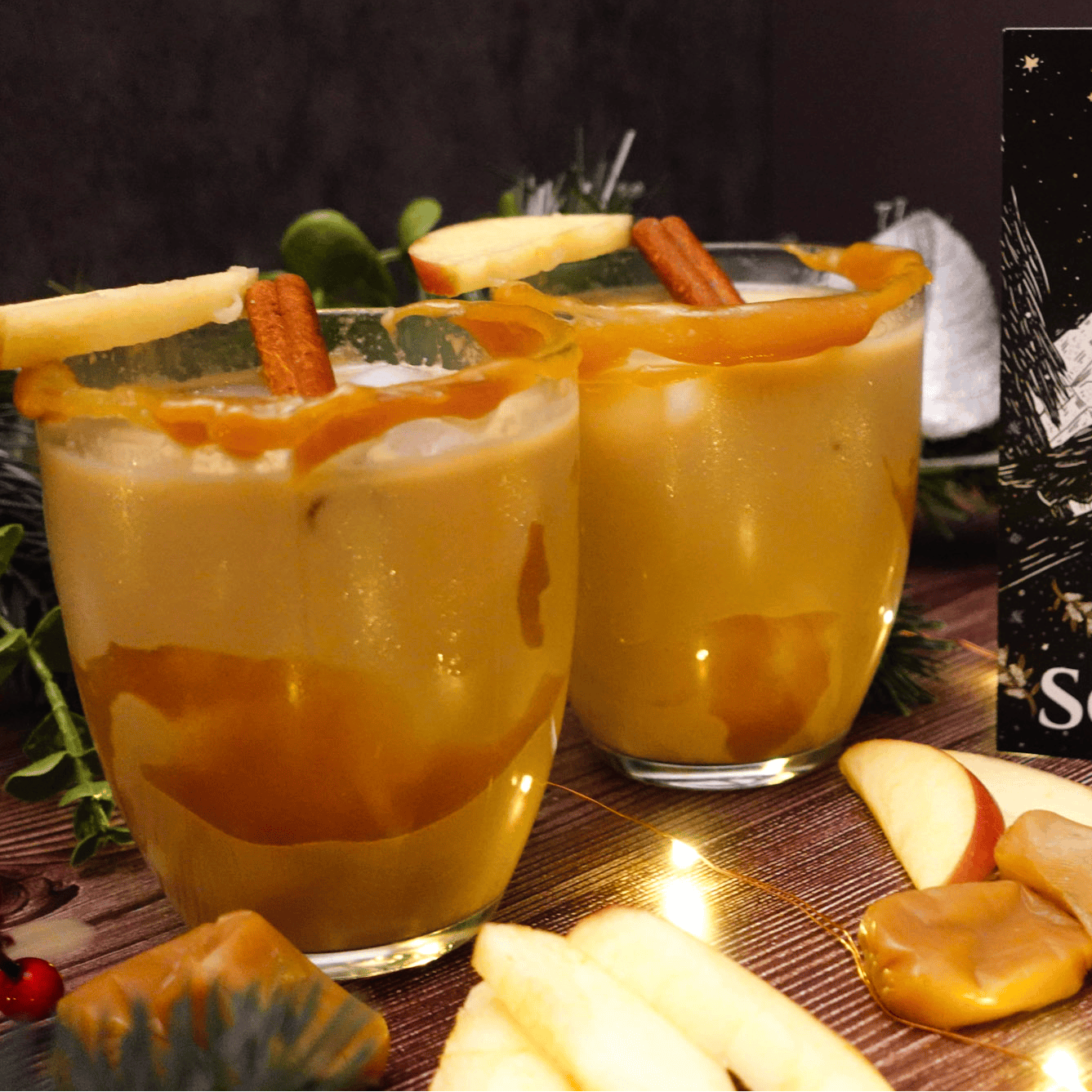 Two glasses of a warm beverage with cinnamon sticks and apples, next to a 'Winter Solstice' card on a festive table.