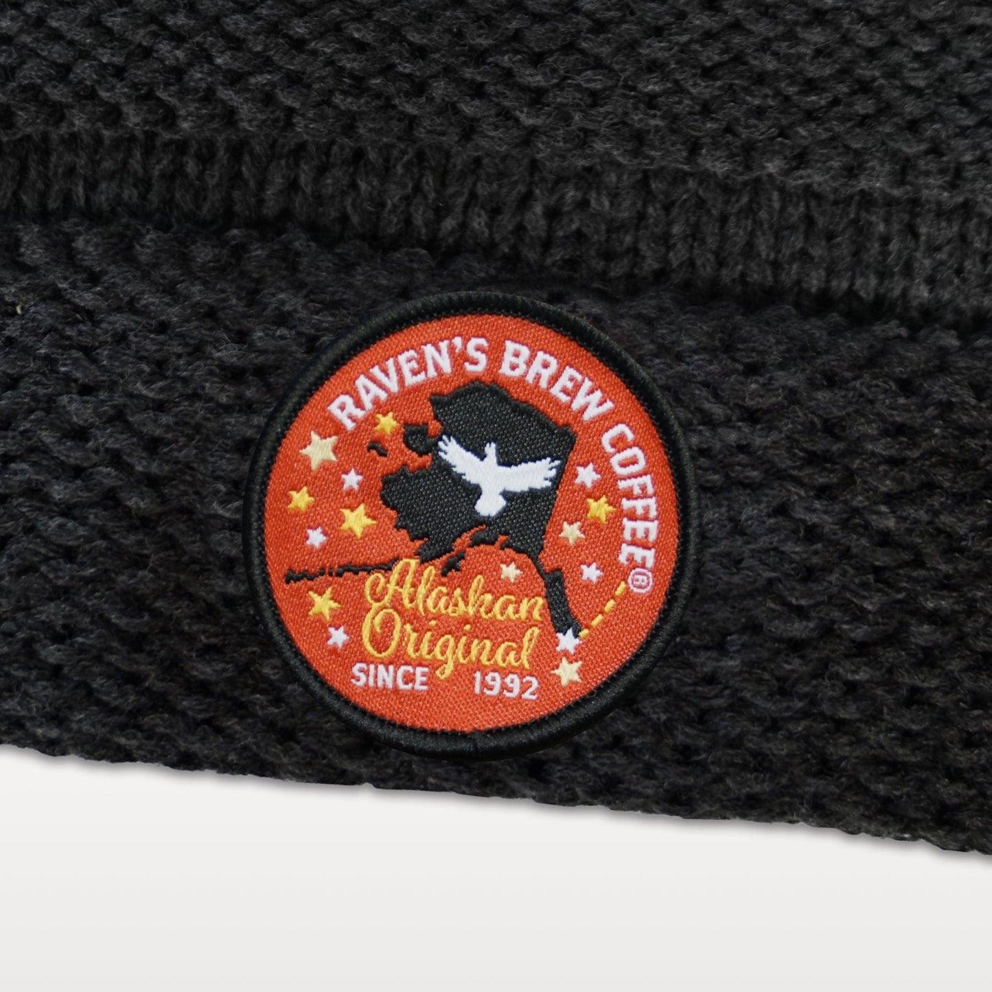 Close up of the round Raven's Brew Coffee embroidered patch featuring a raven, stars and a silhouette of Alaska with the words "Alaskan Original Since 1992" emblazoned at the bottom.
